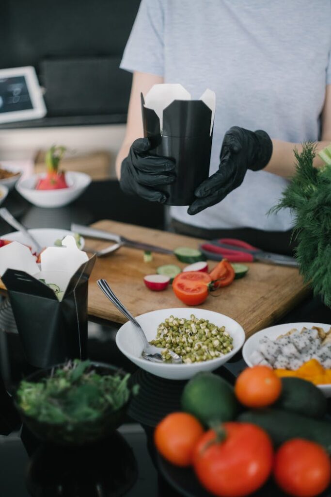 Chef in gloves preparing takeout with fresh veggies and ingredients.
