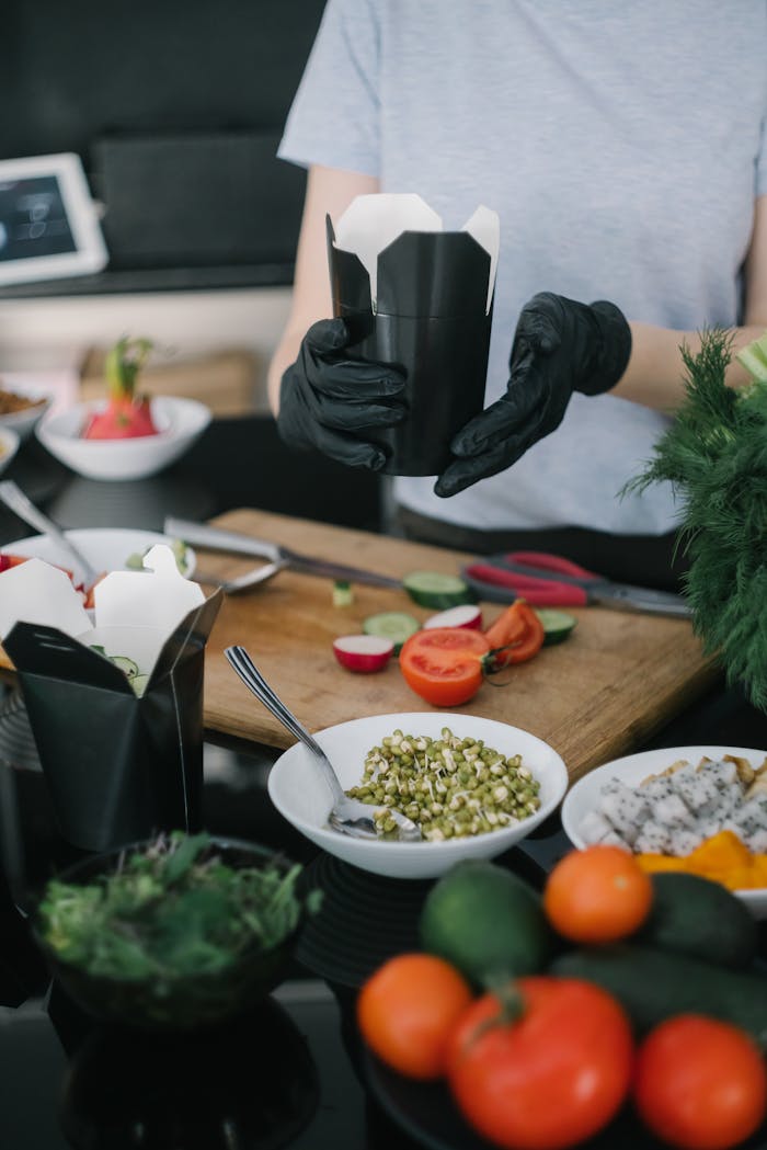 Chef in gloves preparing takeout with fresh veggies and ingredients.